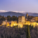 Blick vom Mirador de San Nicolas auf Alhambra und die schneebedeckten Berge der Sierra Nevada in der Abenddämmerung, Granada, Andalusien, Spanien | View from Mirador de San Nicolas to the palace and fortress complex Alhambra and the snow-covered Sierra Nevada mountains at dusk, Granada, Andalusia, Spain